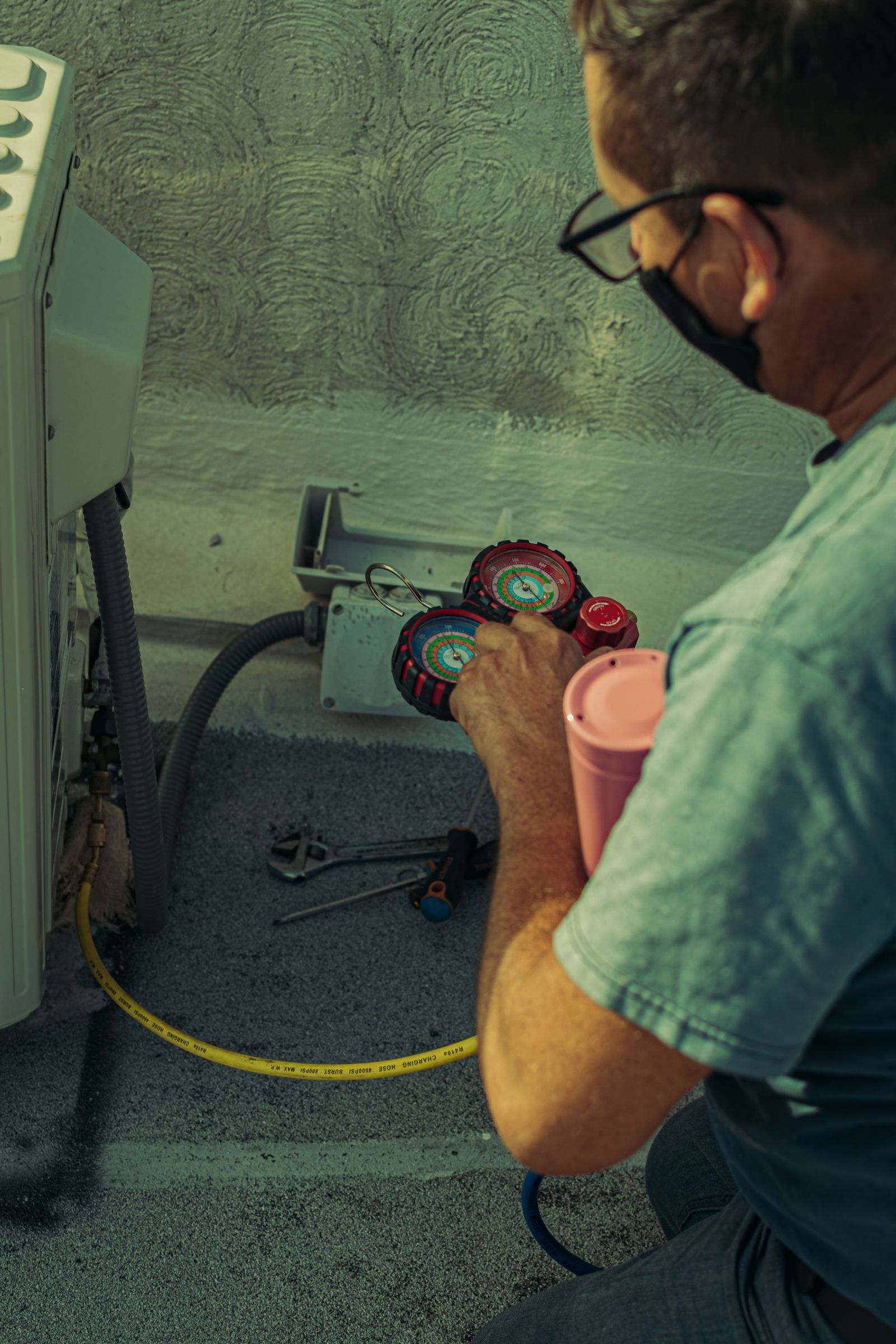 A technician reading refrigerant pressure gauges beside an outdoor air conditioning unit